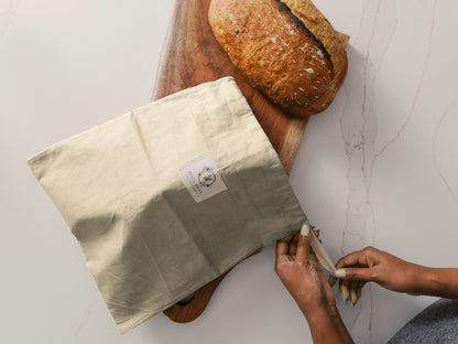 Bee's Wraps Bread Bag with a loaf of bread on a cutting board on top of a marble white countertop.